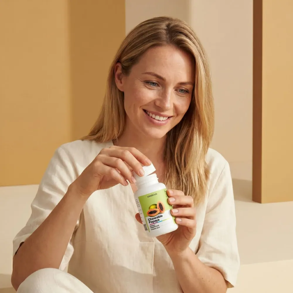 Woman enjoying Chewable Papaya supplement, holding the bottle in a bright, minimalistic setting.