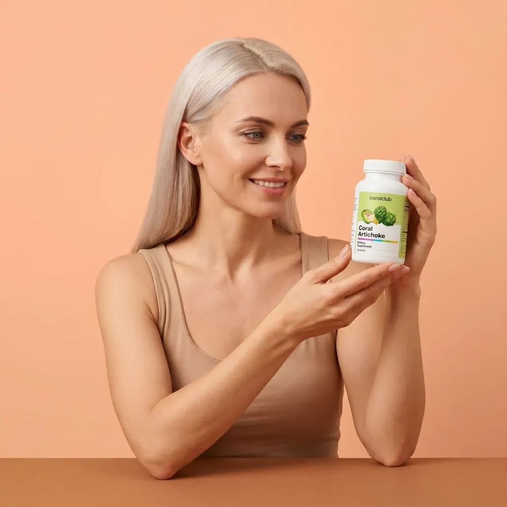 Woman holding Coral Artichoke supplement bottle against a peach background.