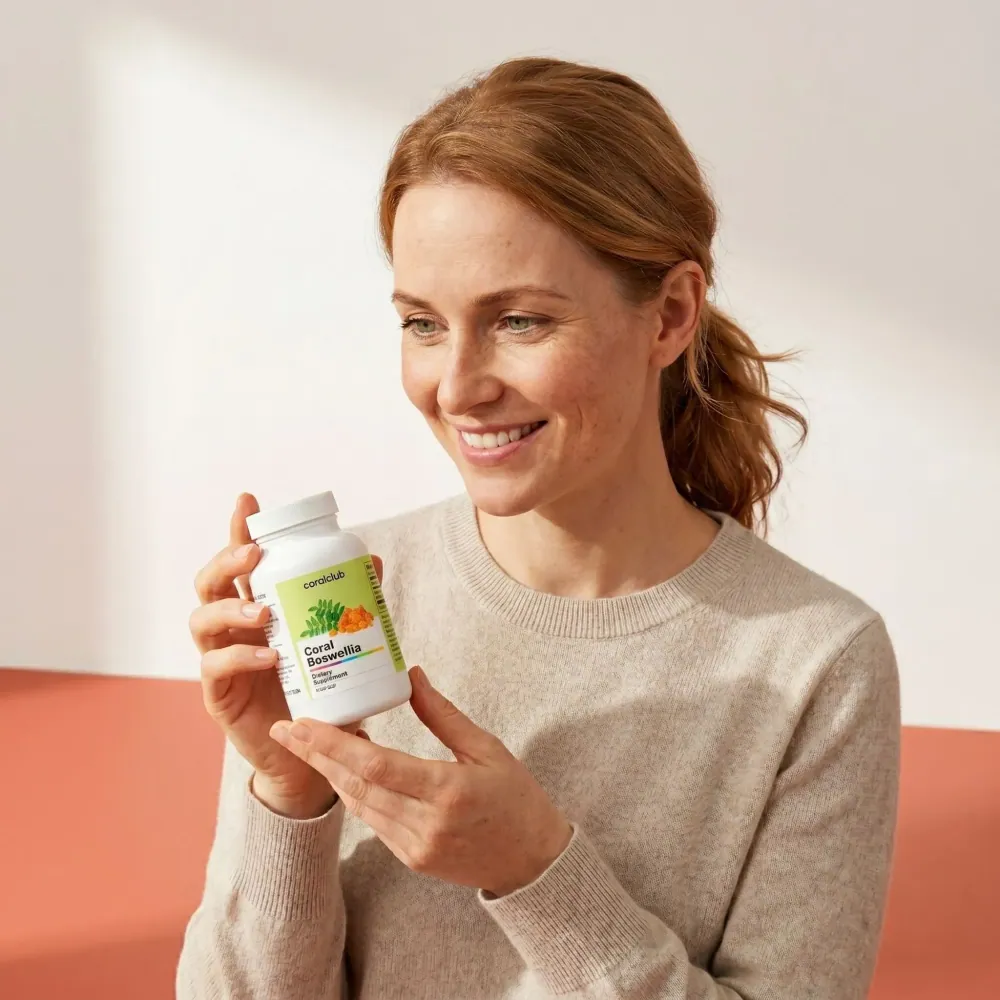 Woman smiling while holding a bottle of Coral Boswellia dietary supplement in a bright lifestyle setting.