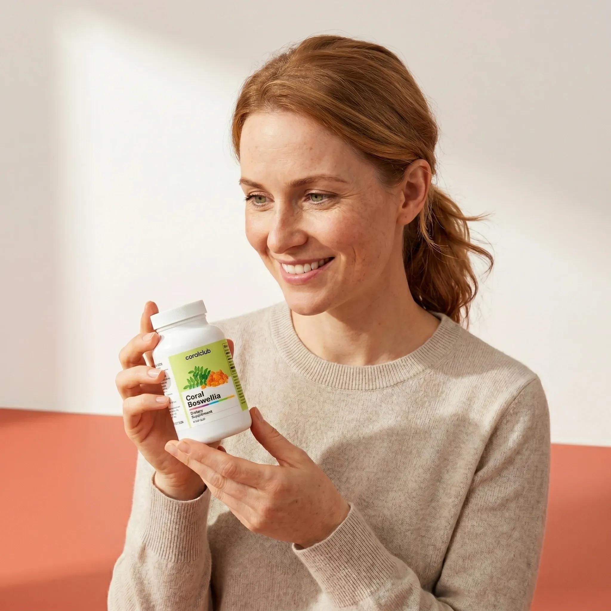 Woman smiling while holding a bottle of Coral Boswellia dietary supplement in a bright lifestyle setting.