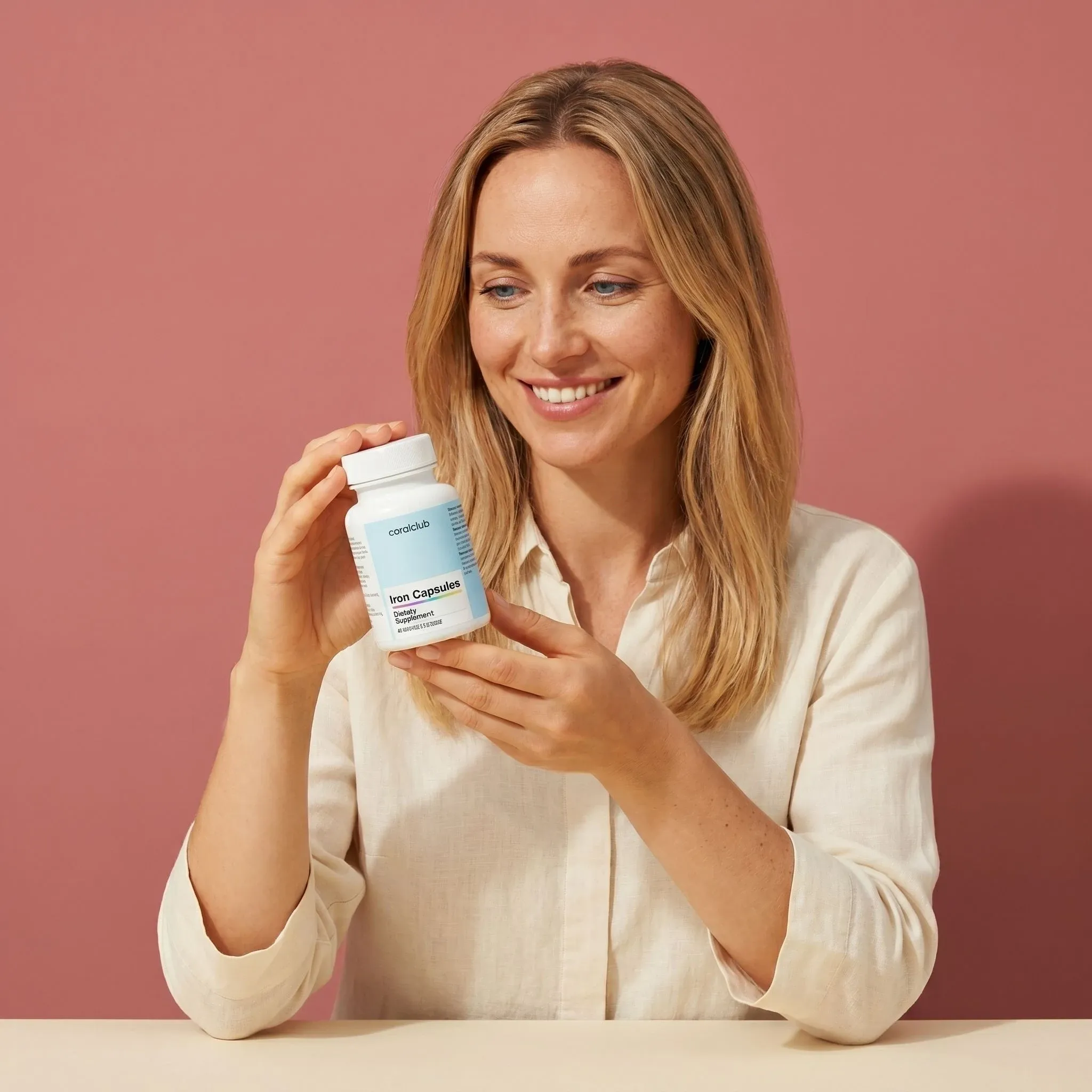 Woman holding a bottle of Iron supplement against a pink background.